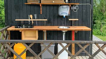 Een houten buitenkeuken met een barbecue, planken en een spoelbak.