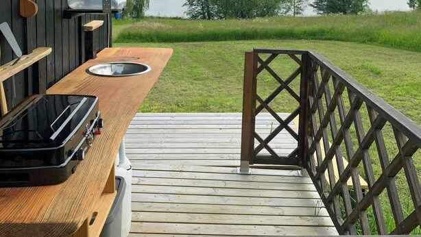 A wooden deck with a metal railing, a table with a sink, and a portable grill. - Wagon with view over Lake Ollerup (Vester Skerninge)
