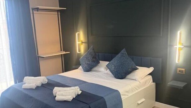 A neatly made bed with a dark blue bedspread, two pillows, and a white bedside table. - Pisacane Family Sea (Naples)
