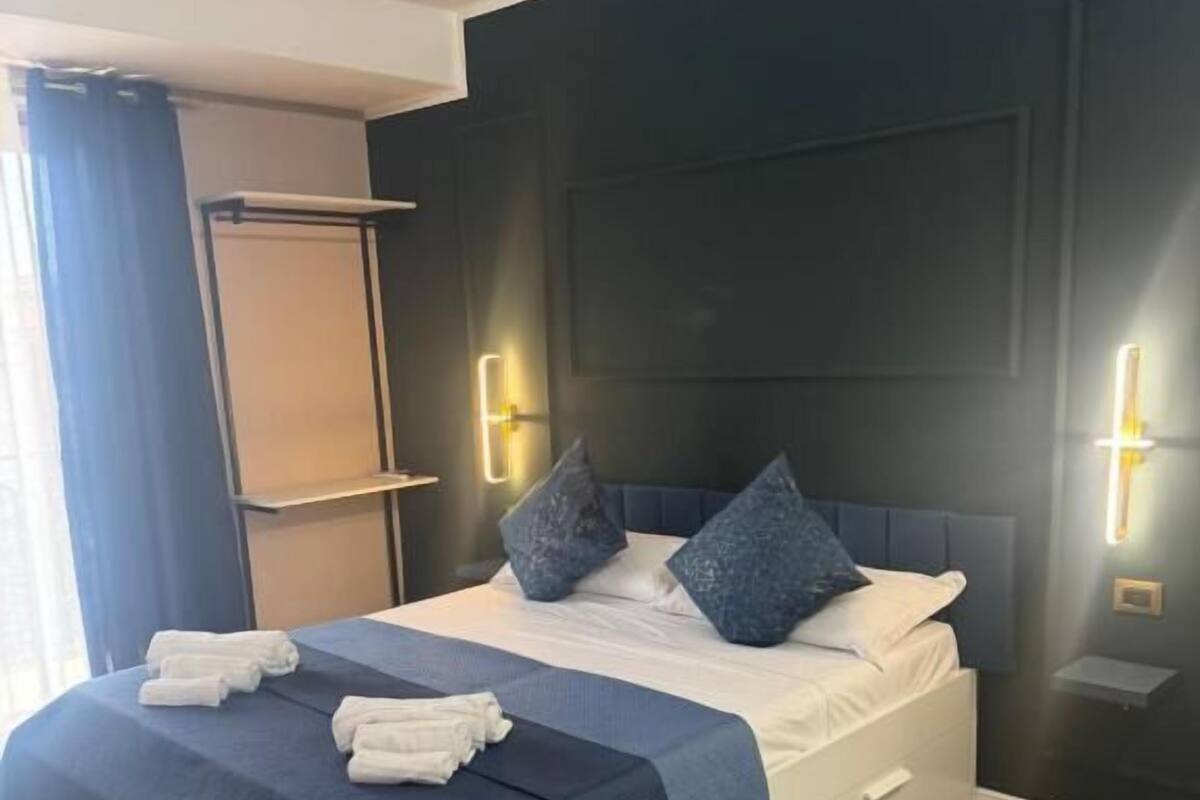 A neatly made bed with a dark blue bedspread, two pillows, and a white bedside table.
