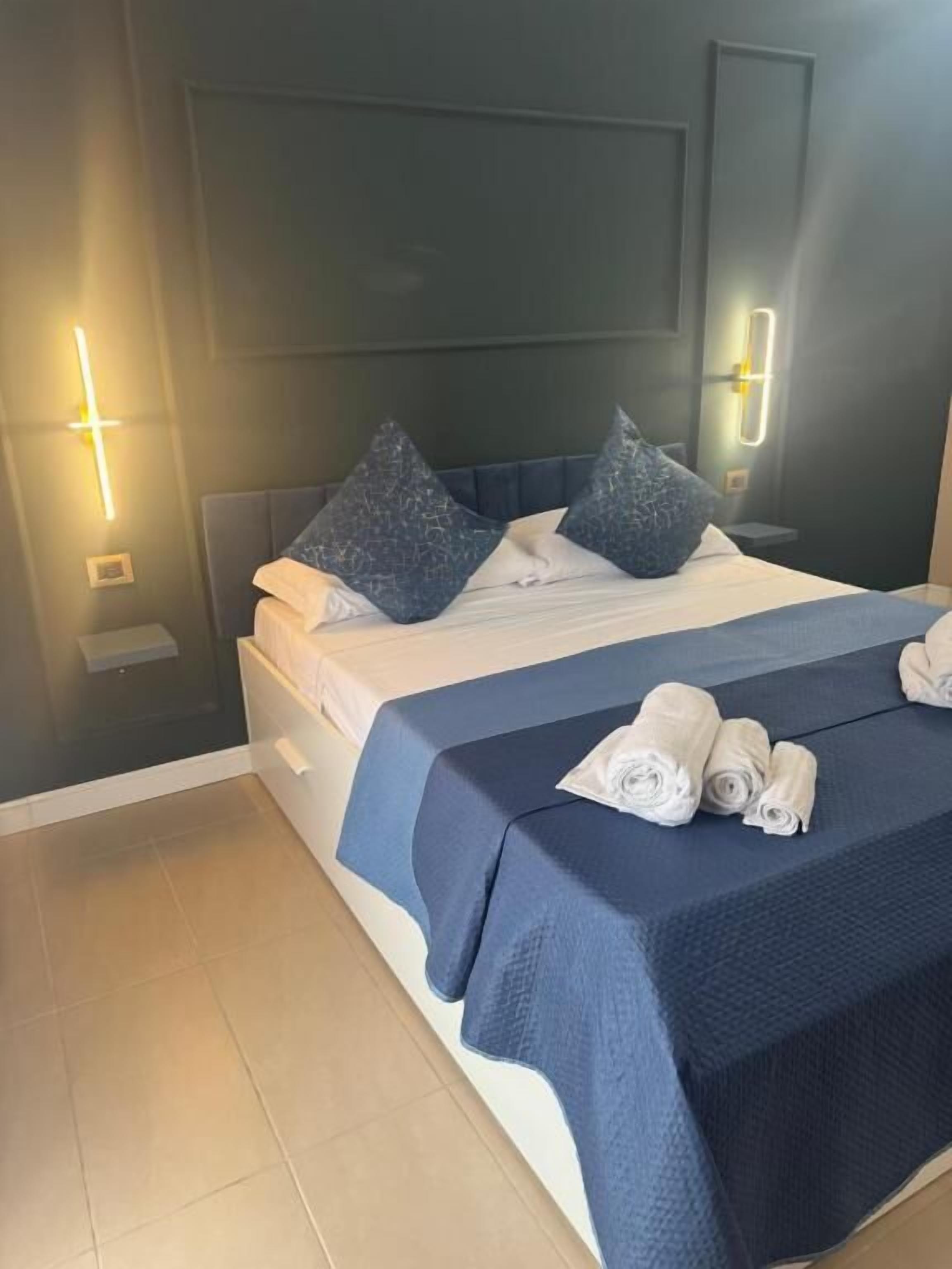 A neatly made bed with pillows and a blue bedspread, two wall-mounted light fixtures, and a folded towel on the bed.