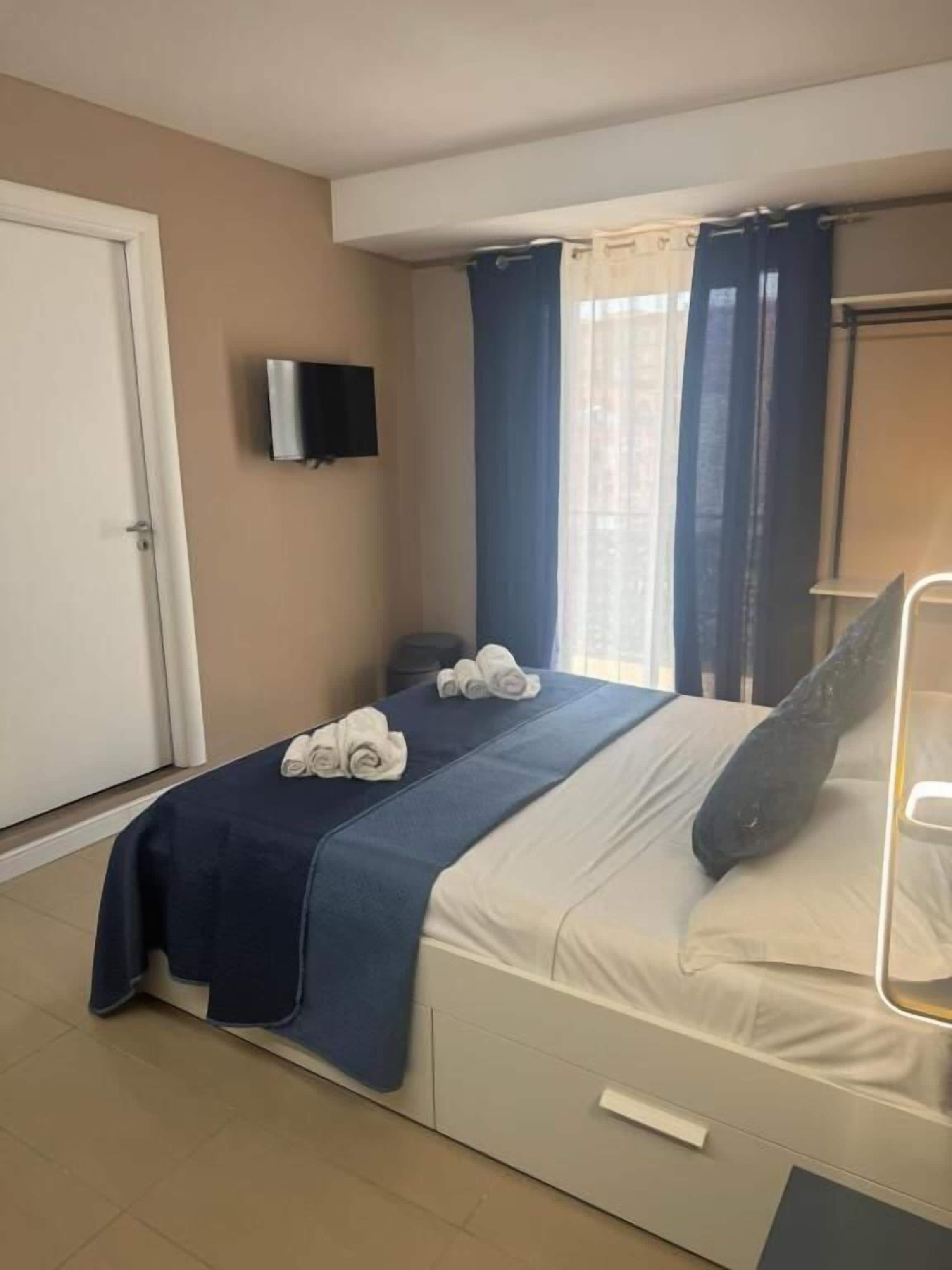 A bedroom with a bed, a TV, a window with curtains, and a door.