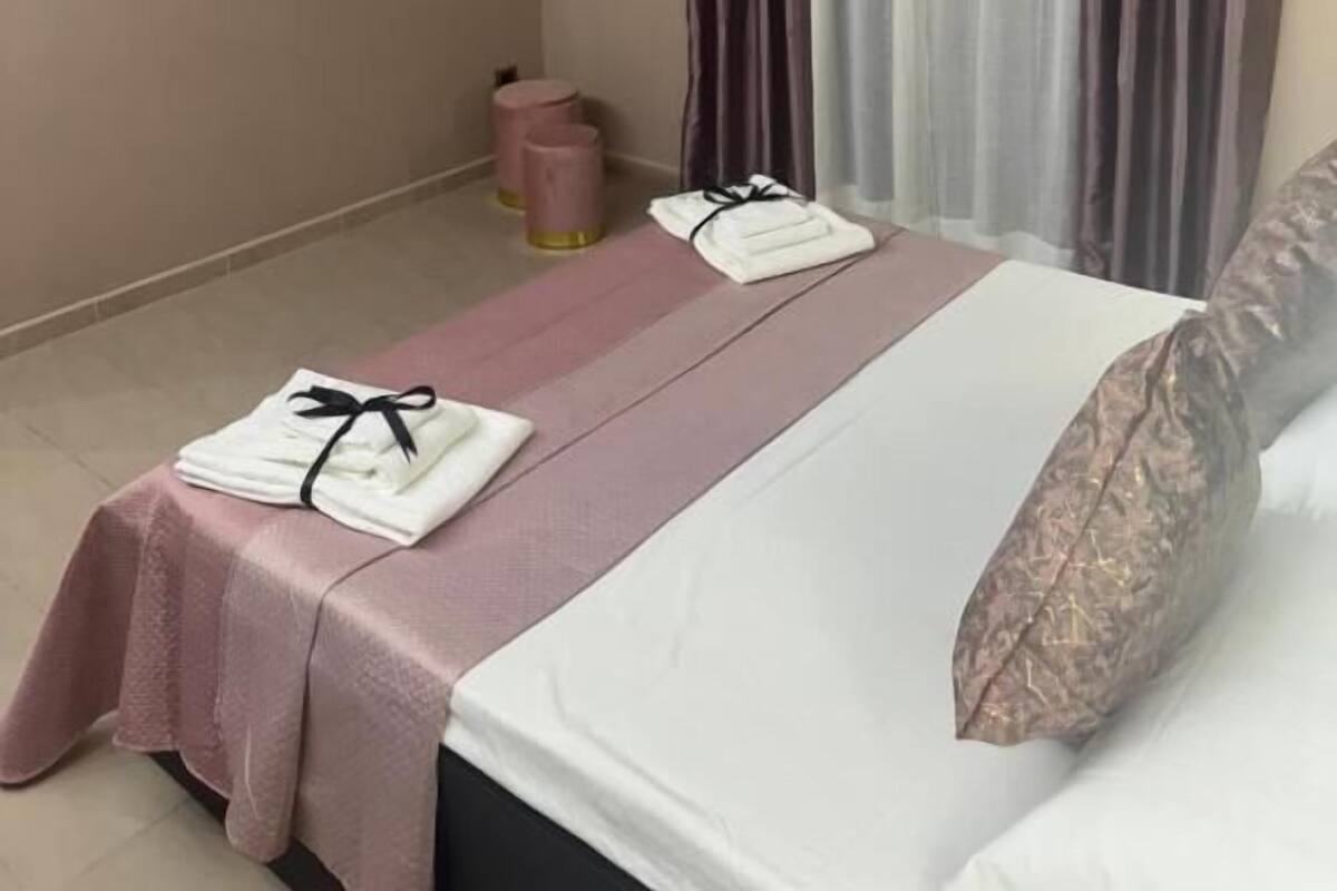 A hotel room with a bed, a television, a window with curtains, and a small table with towels.