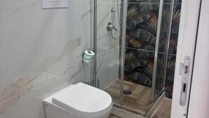 A bathroom with a glass shower enclosure, a toilet, and a patterned wall. - Pisacane Family Sea (Naples)
