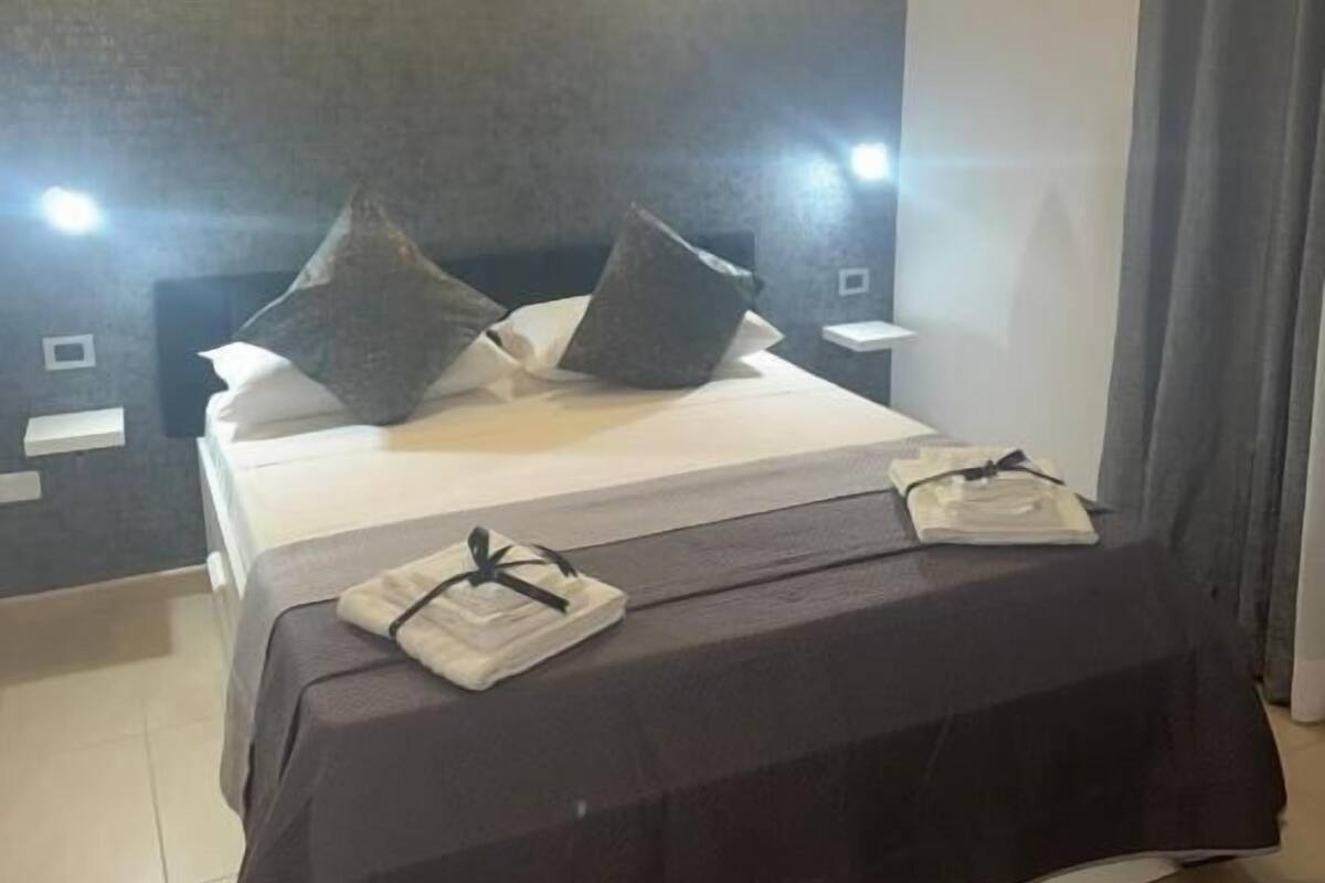 A modern hotel room with a large bed, two bedside tables, and wall-mounted lights.