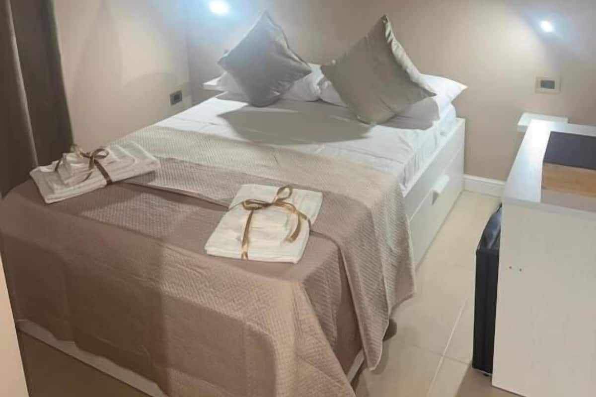 A bedroom with a bed, bedside tables, a nightstand, a lamp, and an air conditioning unit.