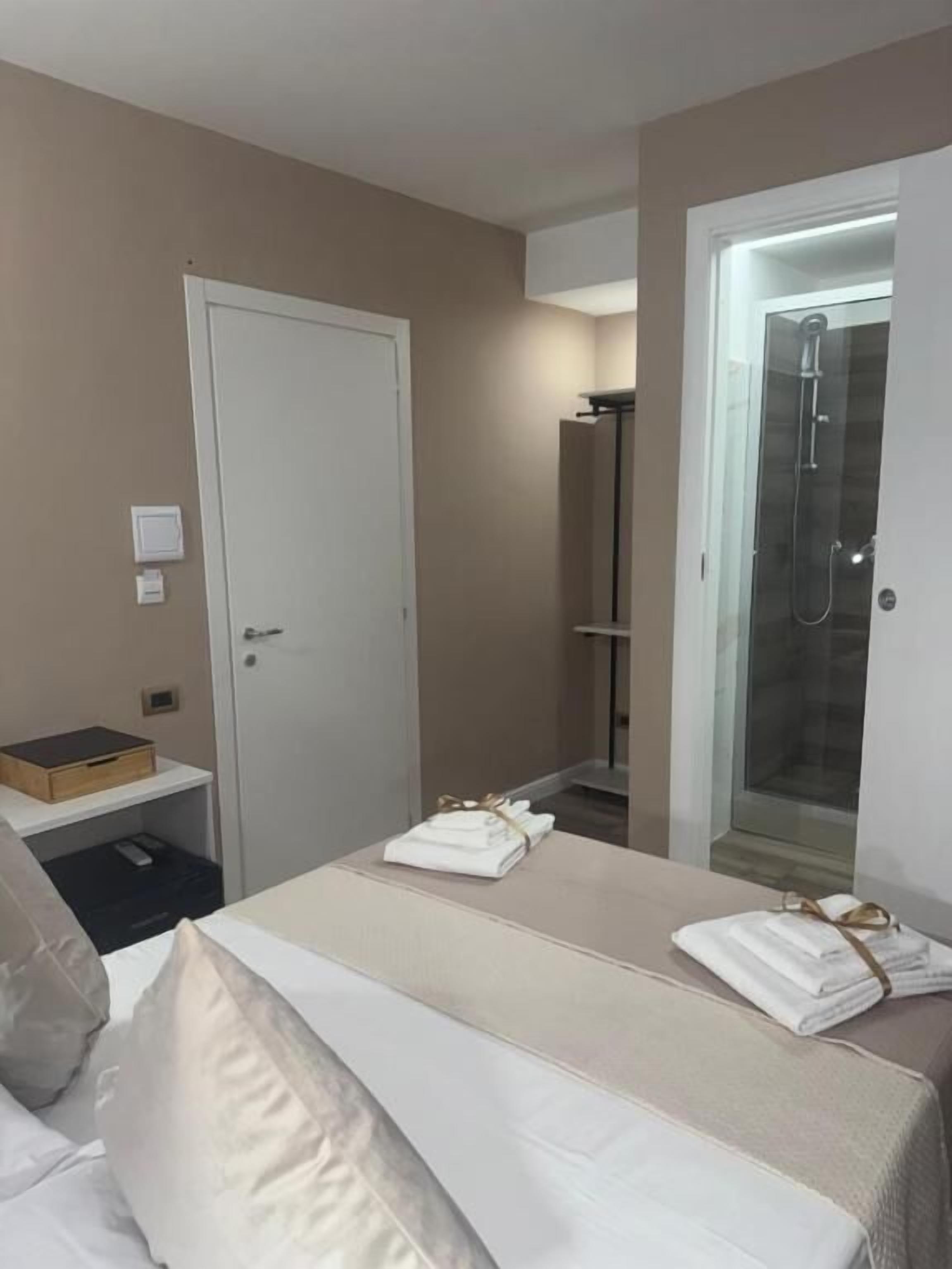 Hotellihuone, jossa on sänky, yöpöytä, vaatekaappi ja suihkutila.