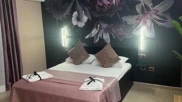Quarto com cama, almofadas, mesa de cabeceira, ar-condicionado fixado na parede e um mural floral.