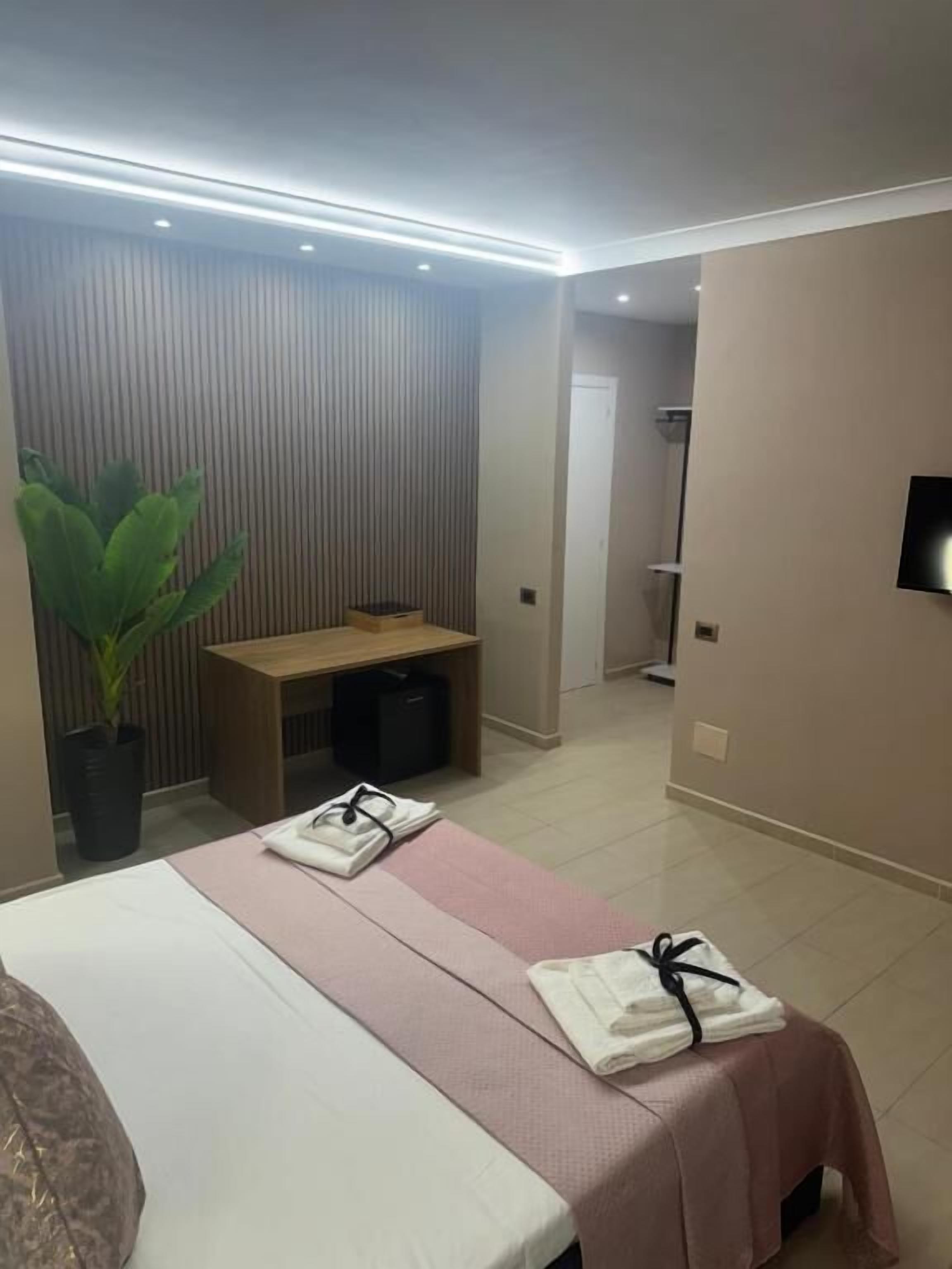 Ein Hotelzimmer mit einem Bett, einem Schreibtisch, einer Zimmerpflanze und einem Fernseher.