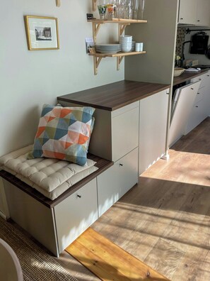A compact kitchen with a wooden countertop, white cabinets, and a built-in bench with a colorful cushion. - Newly built home with outdoor kitchen on Öland (Mörbylånga)
