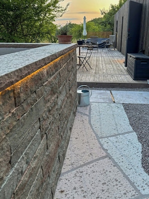 A patio area with a stone wall, outdoor furniture, and a wooden deck. - Newly built home with outdoor kitchen on Öland (Mörbylånga)