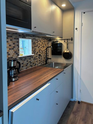 A compact kitchen with a microwave, coffee maker, and hanging pot. - Newly built home with outdoor kitchen on Öland (Mörbylånga)