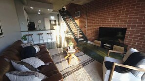 Ein Wohnzimmer mit einer Couch, einem Couchtisch, einem Fernseher und einer Treppe, die zur Küche führt.