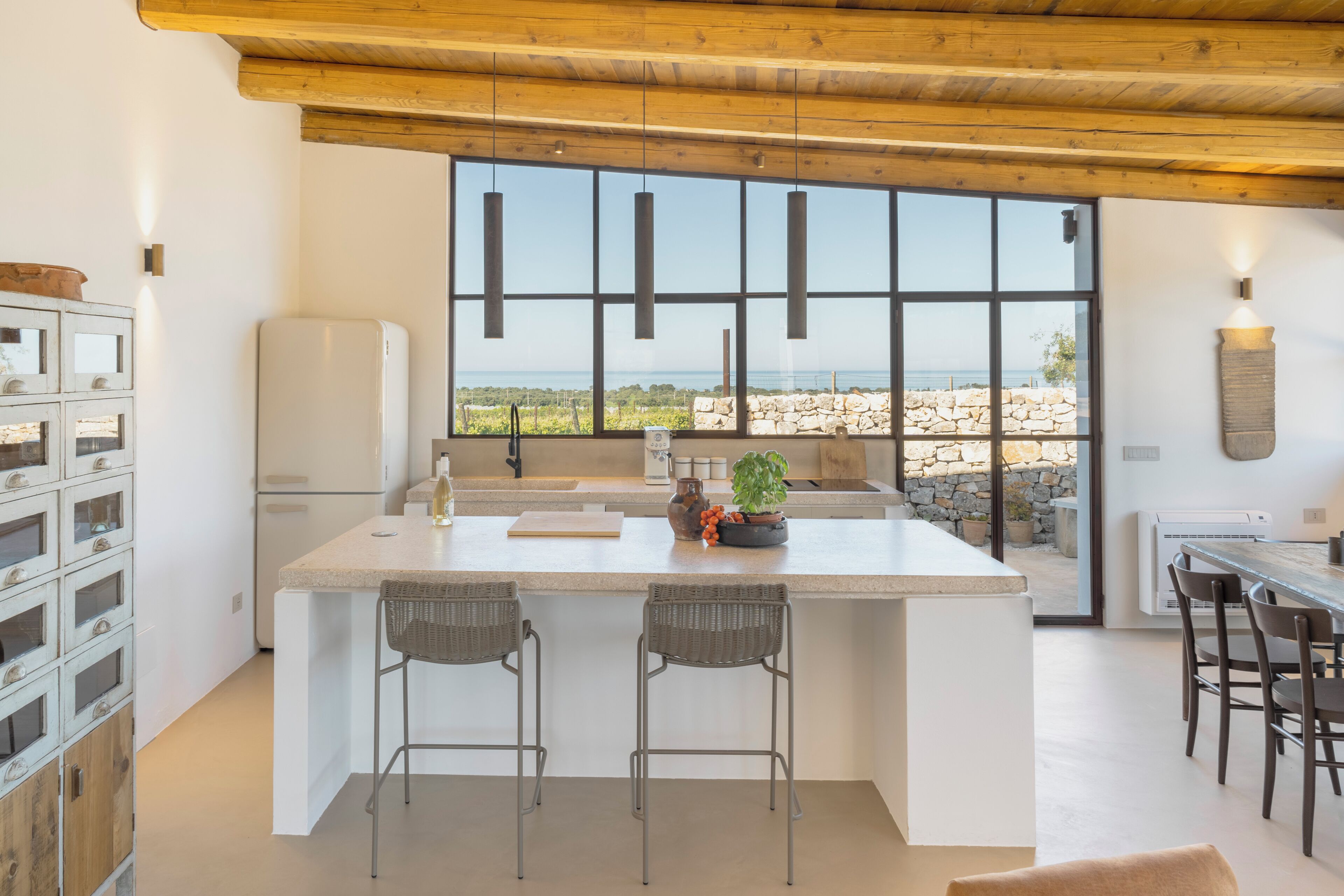 Una cocina moderna con una isla grande, taburetes de bar, una pared de piedra y vista al mar.