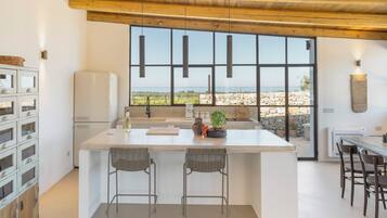 Una cocina moderna con una isla grande, taburetes de bar, una pared de piedra y vista al mar.