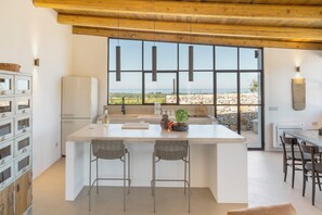Una cocina moderna con una isla grande, taburetes de bar, una pared de piedra y vista al mar.