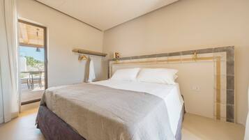 A bedroom with a bed, a window, a door, and a small table with chairs.