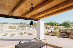 Un patio al aire libre con techo de madera, una lámpara colgante y vistas a un jardín ajardinado.