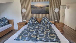 Un lit double avec une couvre-lit à motifs, deux tables de chevet, un tableau accroché au mur et une tête de lit en bois.