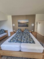 Uma cama de casal com colcha estampada, duas mesas de cabeceira, um quadro na parede e um painel de cabeceira de madeira.