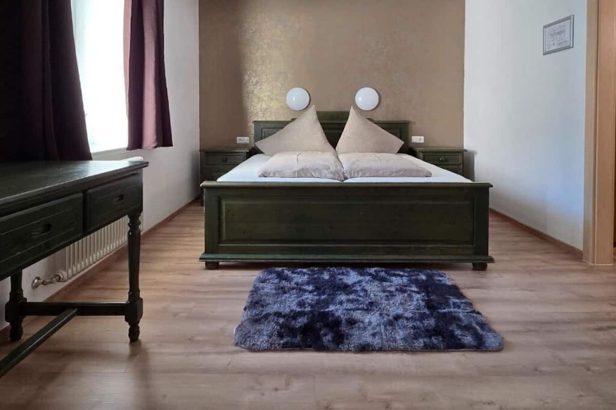 A bedroom with a bed, a dresser, a window with curtains, and a blue rug.