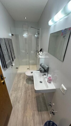 A bathroom with a glass-enclosed shower, a toilet, a sink with a mirror, and a towel rack.