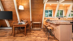 Un intérieur en bois comprenant une table à manger, des chaises, un coin bar et un téléviseur fixé au mur.