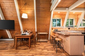 Ein Holzinterieur mit einem Esstisch, Stühlen, einer Bar und einem an der Wand montierten Fernseher.