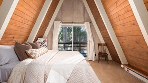 Une chambre avec un plafond en pente, un lit avec plusieurs oreillers, une chaise et une fenêtre avec des rideaux.