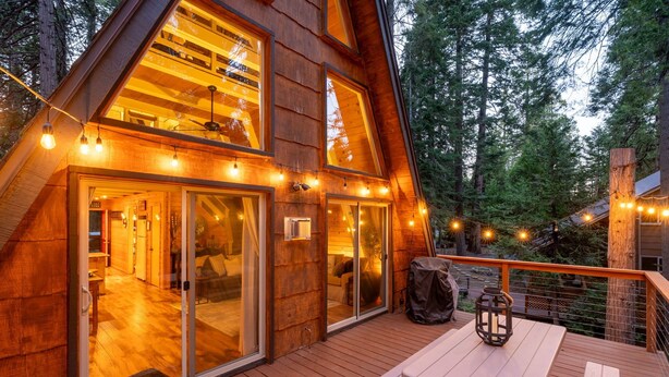 Une cabane en bois dotée d’une terrasse, de grandes fenêtres et de guirlandes lumineuses.