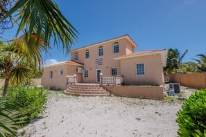 Ein zweistöckiges Gebäude mit Balkon und einem Schild, auf dem 'Golden Pelican Villa' steht, vor einem sandigen Untergrund.