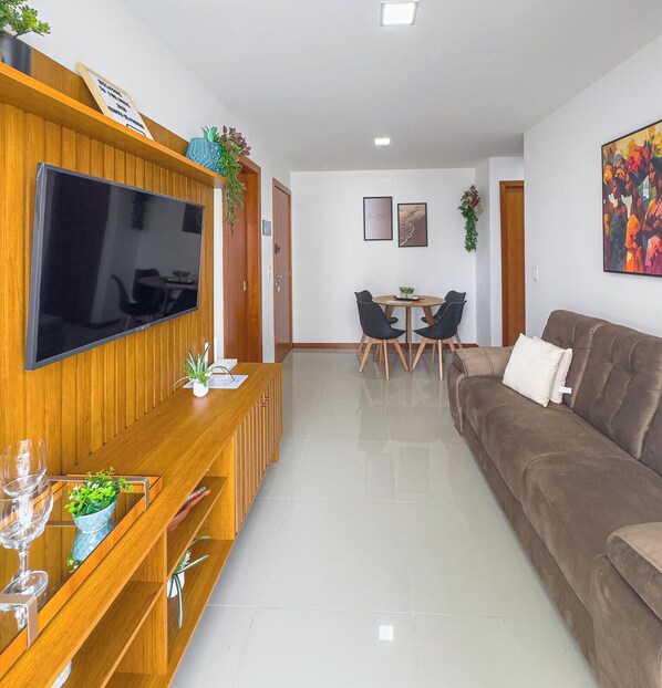 Ein modernes Wohnzimmer mit Flachbildfernseher, einer Holzunterhaltungsecke, einem braunen Sofa, einem Essbereich mit Tisch und Stühlen sowie einem farbenfrohen, abstrakten Gemälde an der Wand.