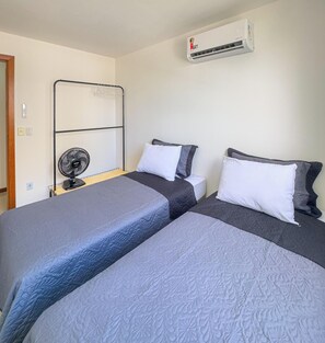 Ein Zimmer mit zwei Betten, einem Standventilator, einer Klimaanlage und einem Metallregal.