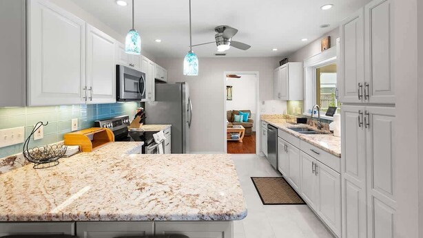 Une cuisine moderne avec des meubles blancs, des plans de travail en granit, un four à micro-ondes et un ventilateur de plafond.
