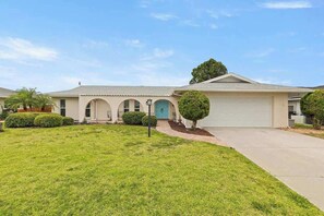 Une maison de plain-pied avec un garage, une pelouse devant et un petit arbre.