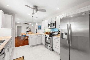 Une cuisine moderne avec des armoires blanches, des appareils en acier inoxydable et un ventilateur de plafond.