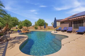 A clear swimming pool with lounge chairs and umbrellas, surrounded by a landscaped garden.