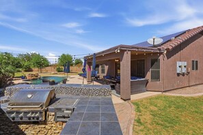 A backyard with a barbecue grill, outdoor seating, a pool, and a covered patio area.
