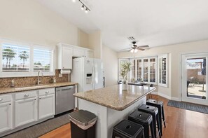 A kitchen with white cabinets, granite countertops, a central island, and a ceiling fan.