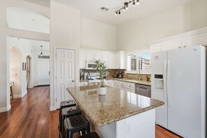 A kitchen with white cabinets, a granite countertop, a refrigerator, and a potted plant.