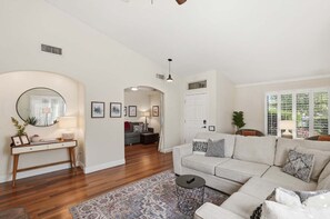 A living room with a sofa, a coffee table, a console table with a lamp, and a large window.