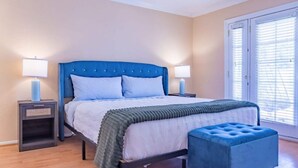 Ein Schlafzimmer mit einem Bett, Nachttischen, einer Bank und einem Fenster mit Jalousien.