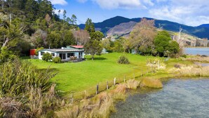 A house with a lawn and a small pond, surrounded by trees and mountains.