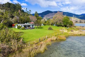 A house with a lawn and a small pond, surrounded by trees and mountains.