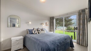 A bedroom with a bed, a nightstand, a mirror, a window with curtains, and a view of the outdoors.