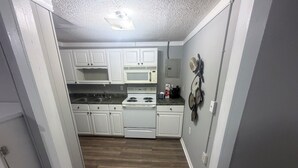 A narrow kitchen with white cabinets, a stove, and a microwave.