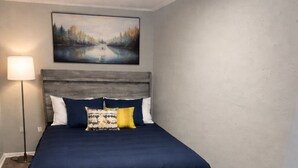 A bedroom with a bed, a nightstand, a lamp, and a painting on the wall.