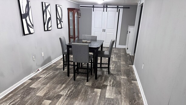 A dining area with a table and chairs, a wooden floor, and a sliding door in the background.