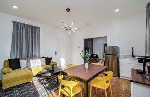 Ein modernes Wohnzimmer mit einer Couch, einem Esstisch mit Stühlen, einer Küchenzeile inklusive Kühlschrank und einer Deckenleuchte.