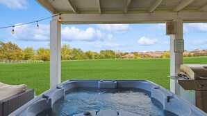 Ein Whirlpool unter einem Überdachung mit Blick auf eine grüne Wiese und Häuser in der Ferne.